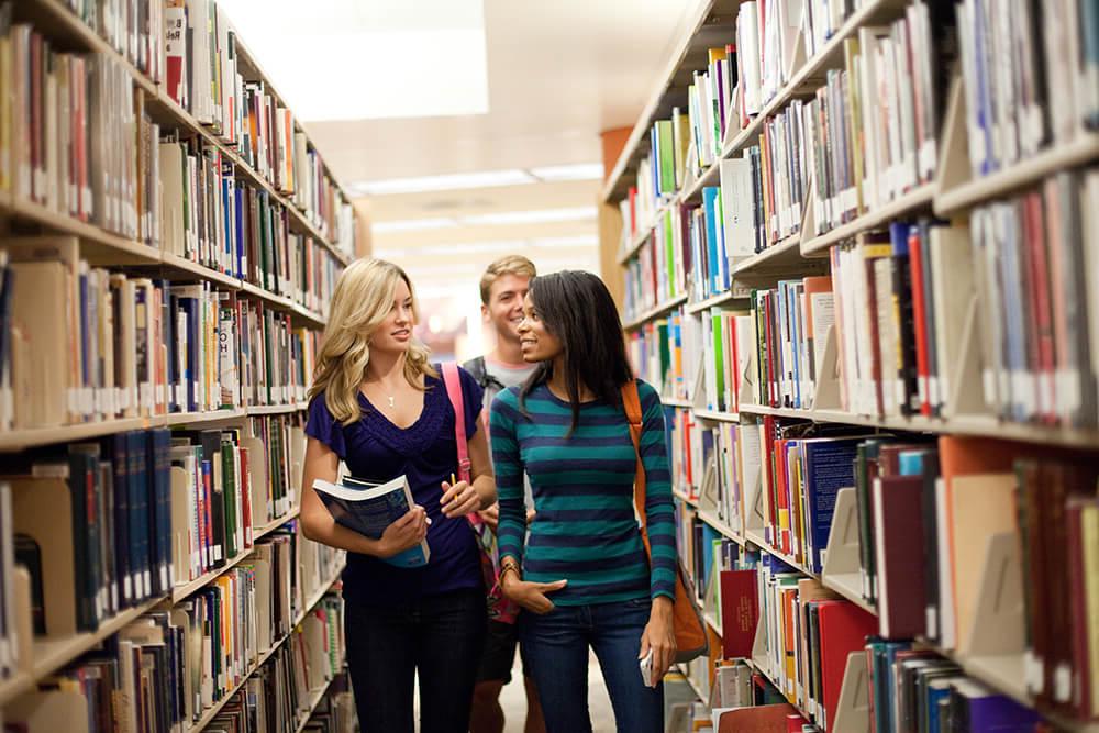 Student in library standing and talking between bookshelves